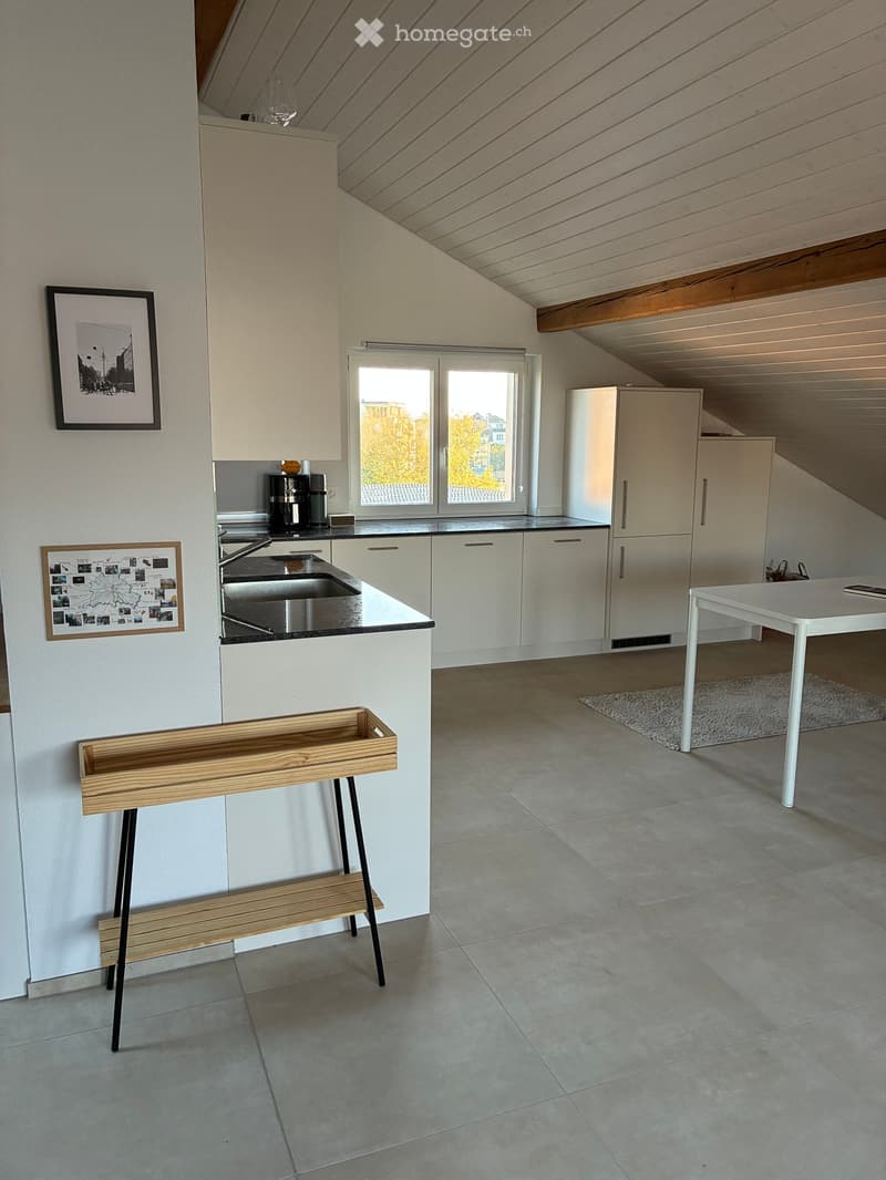 Modern kitchen with white cabinets, stainless steel sink, refrigerator, coffee maker, and a small wooden bench near the wall.