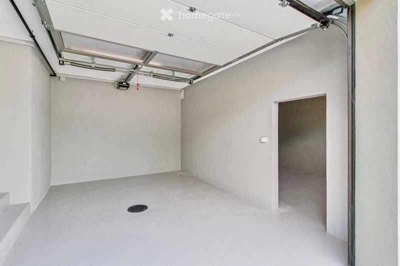 Empty garage with white walls, concrete floor, and a partially open garage door. No furniture or equipment is present.
