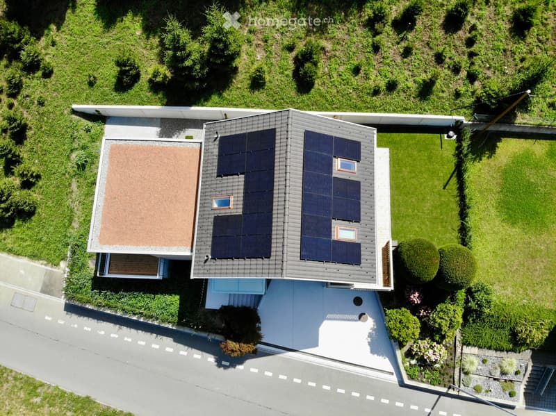 A modern two-story house with solar panels on the roof, surrounded by a well-maintained garden and lawn.