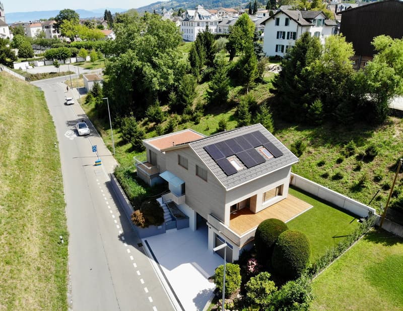 Modern two-story house with solar panels on the roof, a wooden deck, and a well-maintained garden.