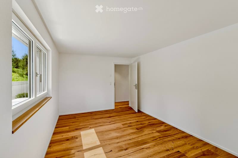 Empty room with wooden flooring, white walls, large windows, and an open doorway leading to another space.