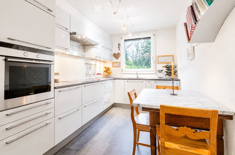 Modern kitchen with white cabinets, stainless steel appliances, a central island with a marble countertop, and wooden chairs.