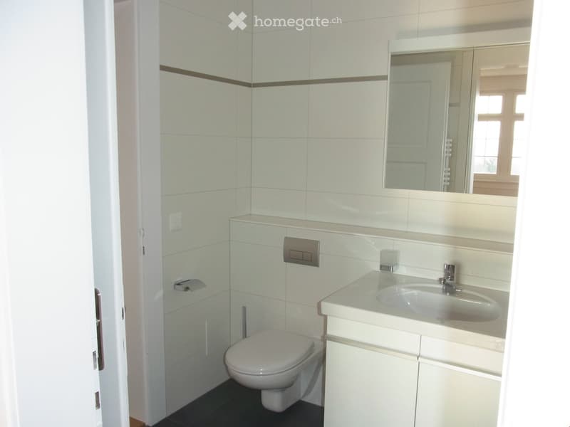 Modern bathroom with white tiles, a toilet, a sink with a mirror, and a cabinet.