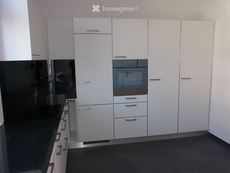 Modern kitchen with white cabinets, stainless steel handles, and a built-in oven. Dark countertops and tiled flooring.
