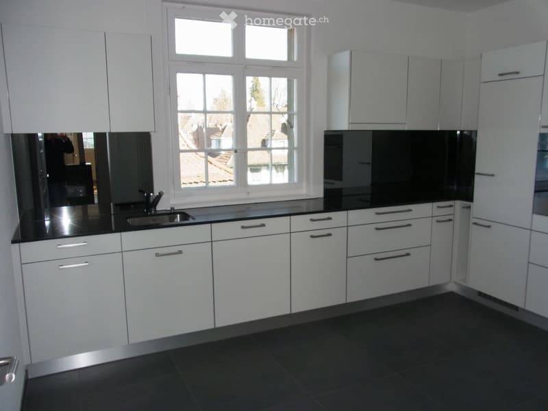 Modern kitchen with white cabinets, black countertops, and stainless steel sink and faucet.