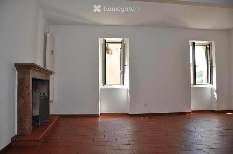 Empty room with terracotta tiled floor, white walls, fireplace, and two open windows letting in natural light.