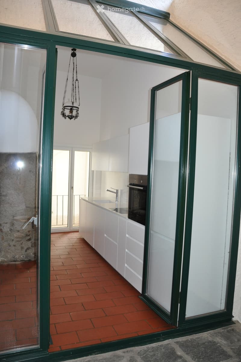 Modern kitchen with white cabinets, a central island, and a brick floor. Features include a hanging chandelier, a sink with a modern faucet, and an oven.