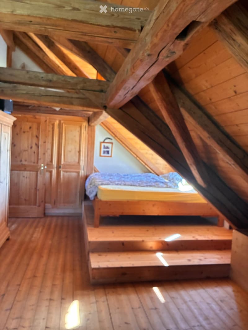 Cozy attic bedroom with wooden beams, slanted ceiling, wooden bed, and wardrobe.
