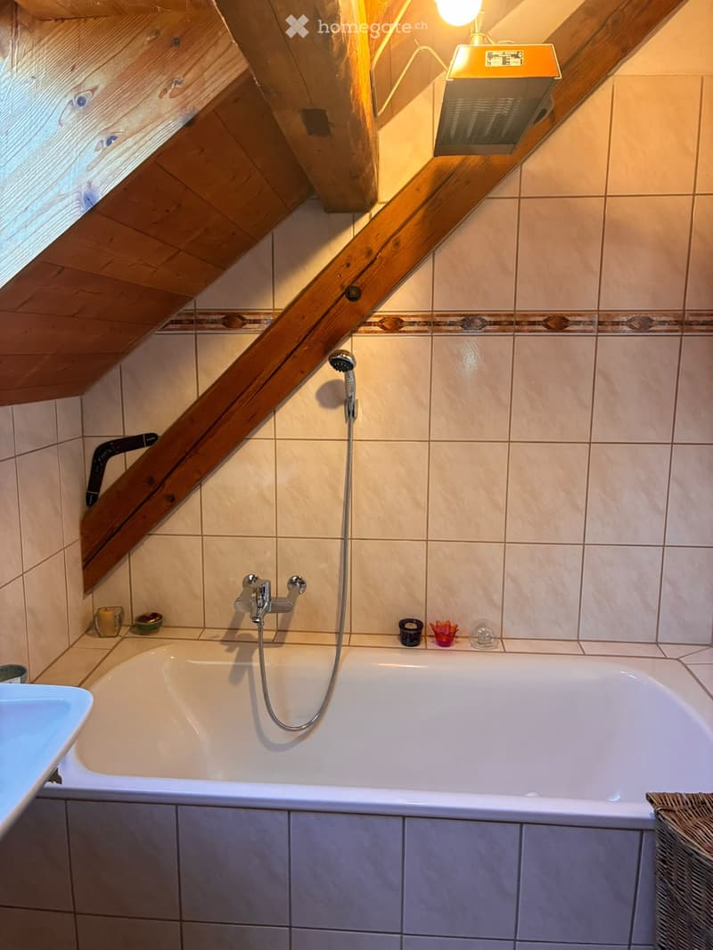 Bathroom with a bathtub, showerhead, faucet, sink, and decorative items on the edge of the tub.