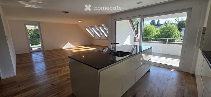 Bright, open kitchen with wooden flooring, modern island, and large windows leading to a balcony.