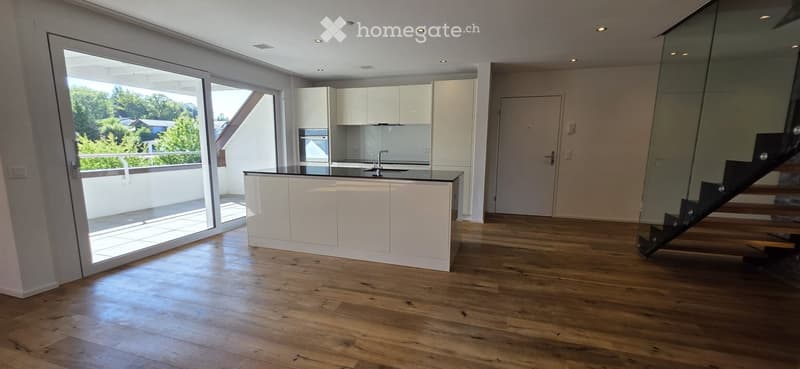 Modern kitchen with white cabinets, wooden flooring, and a large window offering a view of the outdoor area and balcony.