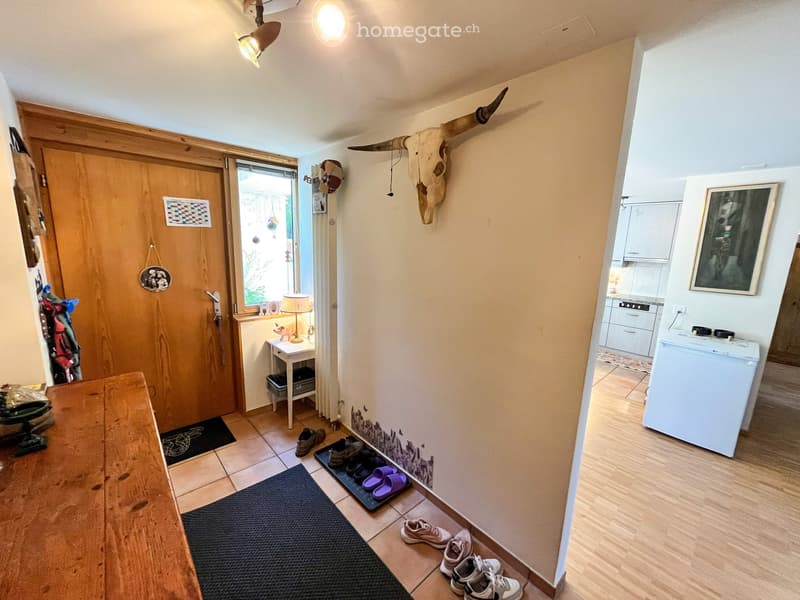 Hallway with wooden door, small table with lamp, shoe rack, and a skull decoration on the wall.