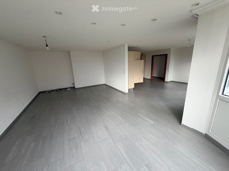 Empty room with grey tiled flooring, white walls, and recessed ceiling lights. A small cabinet is visible in the background.