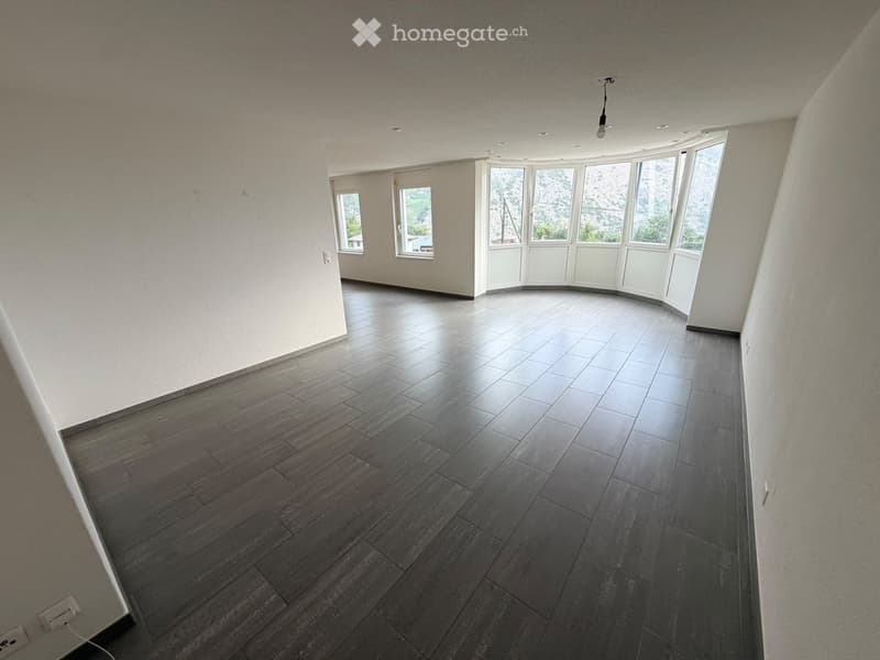 Empty room with wooden flooring, white walls, and large windows offering a scenic view.