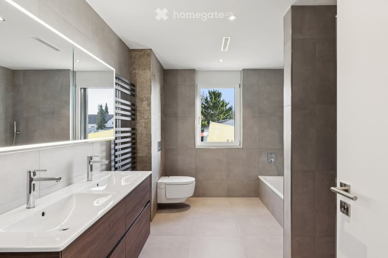 Double sink, toilet, bathtub, grey tiles, natural light from window, minimalist design