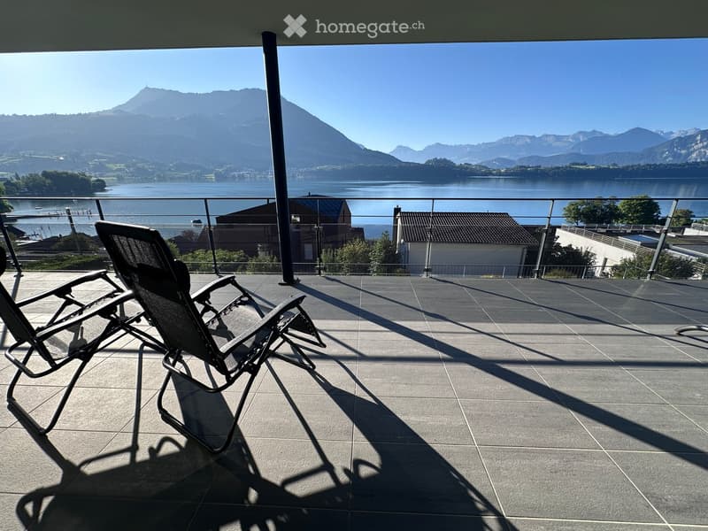 Balcony with two lounge chairs, overlooking a lake and mountains.