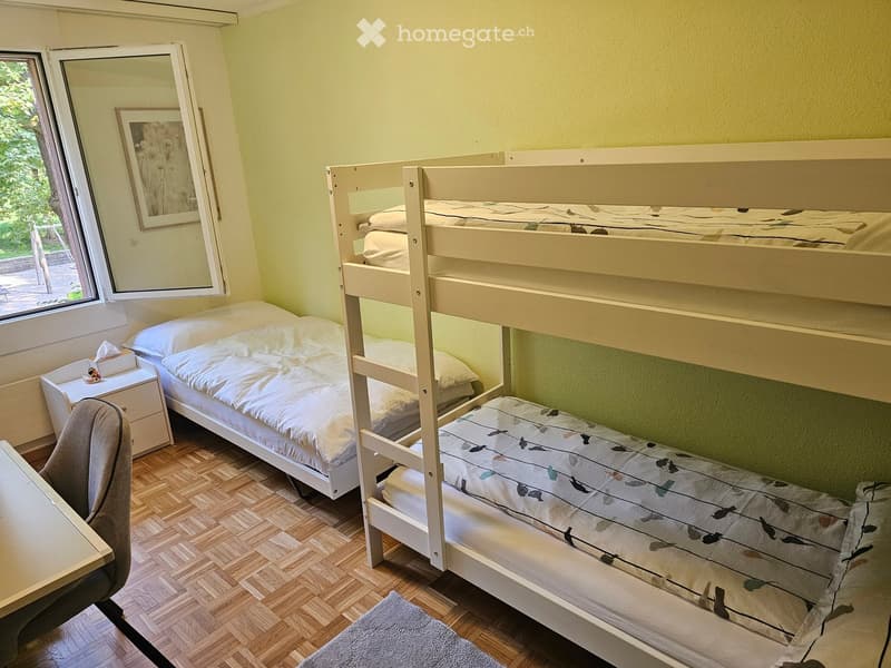 Cozy room with wooden floor, bunk bed, single bed, nightstand, chair, and a mirror with a picture frame.