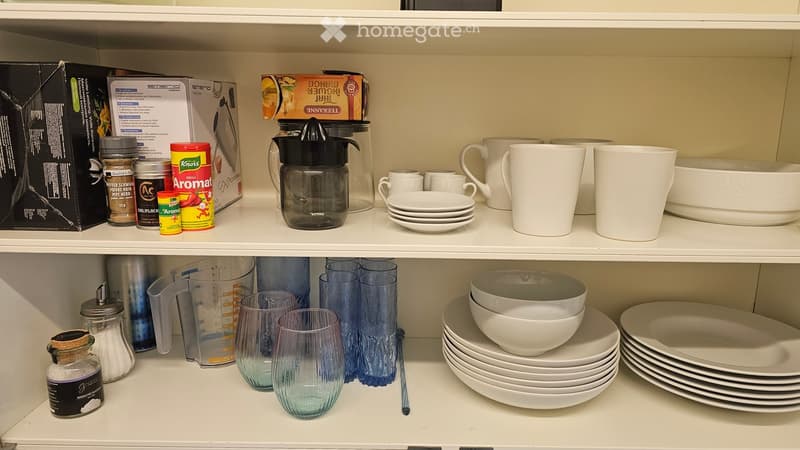 kitchenware on shelves including glasses, bowls, measuring cups, pitchers, and jars