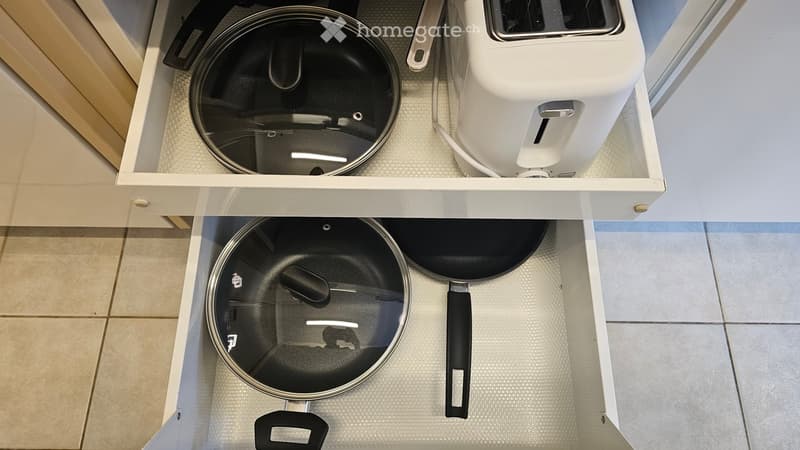 Two drawers of a kitchen with a pot, pans and a toaster inside