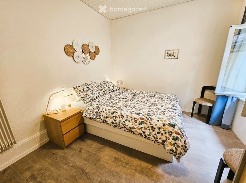 Cozy bedroom with a bed, nightstand, lamp, chair, and decorative wall art.