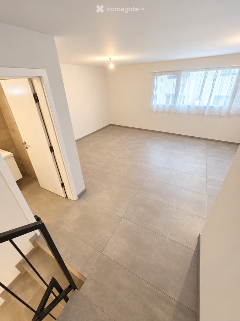Empty room with tiled floor, white walls, and large windows with curtains. A staircase leads to another level.