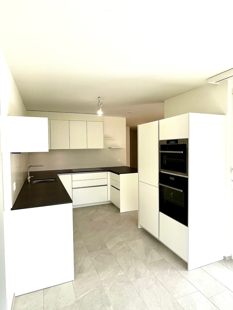 Modern kitchen with white cabinets, black countertops, and built-in ovens. Features a sleek design with a central island and ample storage space.