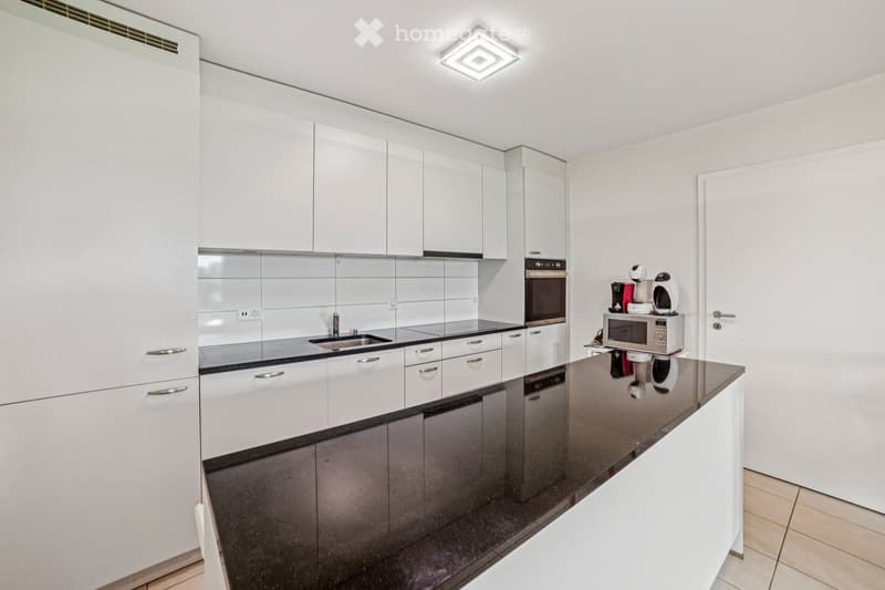 Modern kitchen with white cabinets, black countertops, and stainless steel appliances including a sink, oven, and microwave. A coffee maker is placed on the counter.