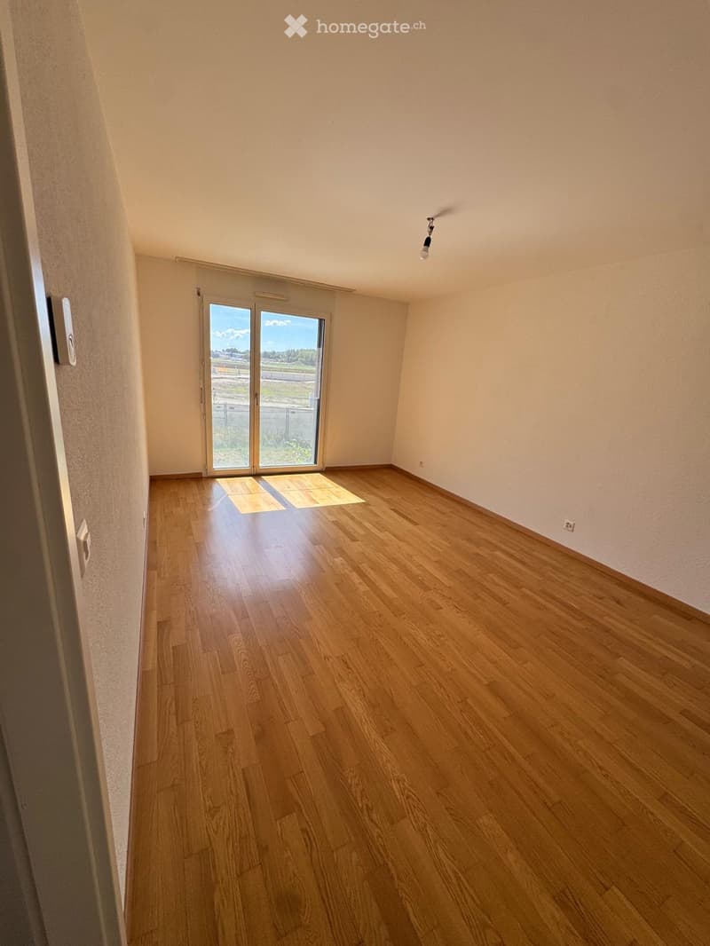Empty room with wooden flooring, large sliding glass door, and natural light. No furniture or equipment present.
