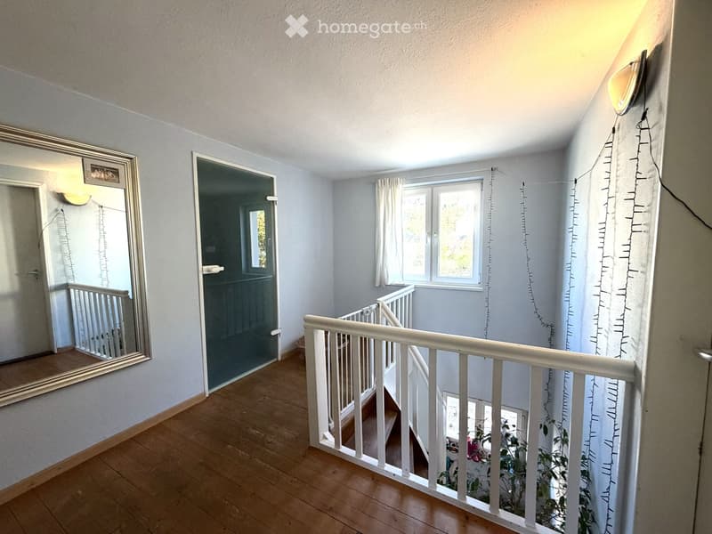 Staircase with wooden flooring, white railing, large mirror on the wall, and a window with white curtains.