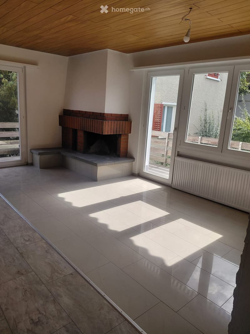 Empty room with tiled floor, fireplace, large windows, and sliding glass doors leading outside.