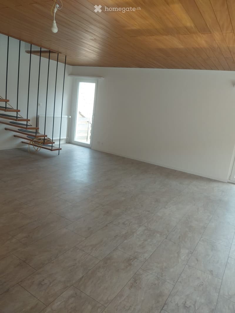 Empty room with wooden ceiling, tiled floor, staircase leading upwards, and a window letting in natural light.