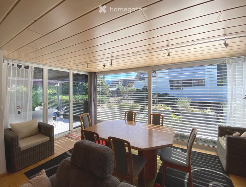 Empty room with light wooden flooring, large windows with blinds, and a view of a pool and outdoor area.