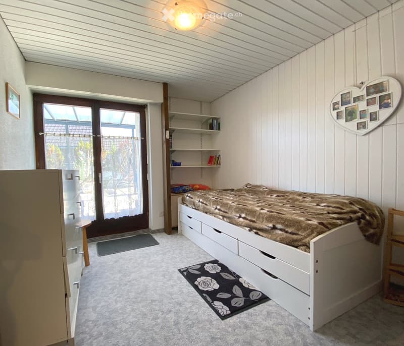 Cozy bedroom with a lofted bed, wooden flooring, shelves, and a large window overlooking a pool area.