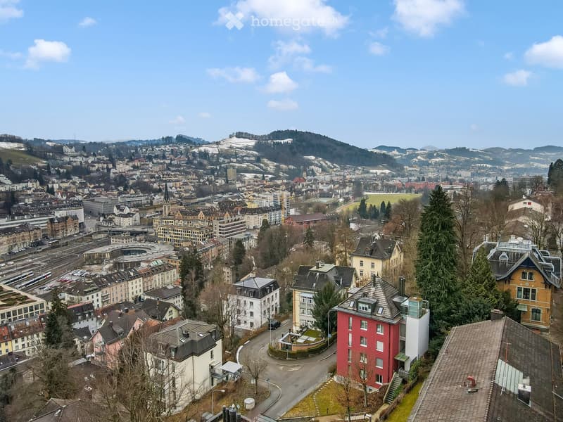 Aerial view of a city with diverse buildings, mountains, and a clear sky.