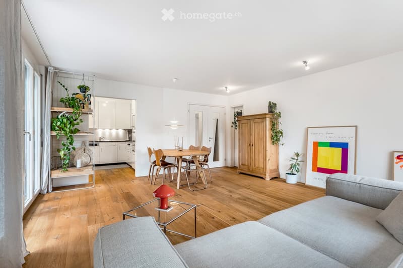 wooden floor, white walls, gray couch, dining table, kitchen visible, plants