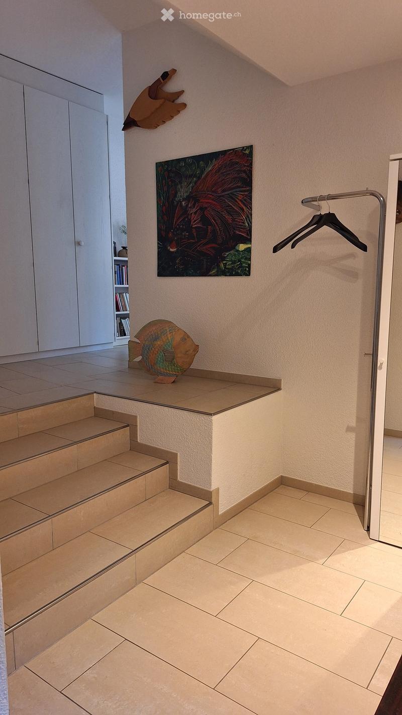 Hallway with tiled floor, staircase, wall-mounted artwork, and coat rack.