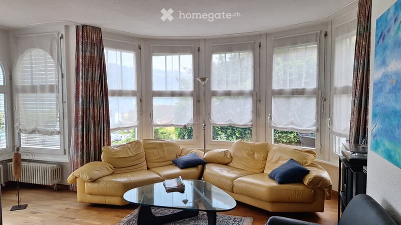 Bright living room with large windows, cream leather sofa, glass coffee table, floor lamp, and artwork on the wall.