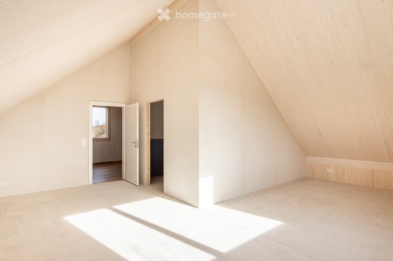 Empty attic room with wooden walls and ceiling, natural light from a window, and two open doors leading to other spaces.