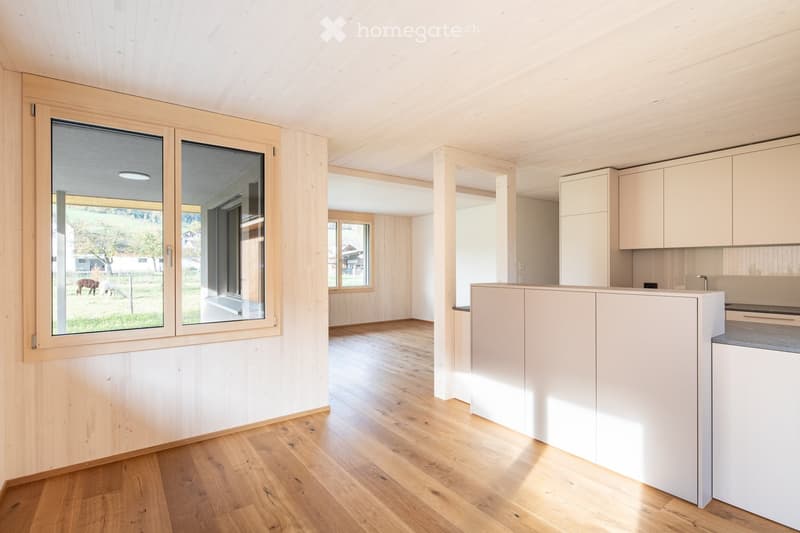 Bright, modern kitchen with light wood cabinets, a white countertop, and large windows overlooking a grassy area with animals.