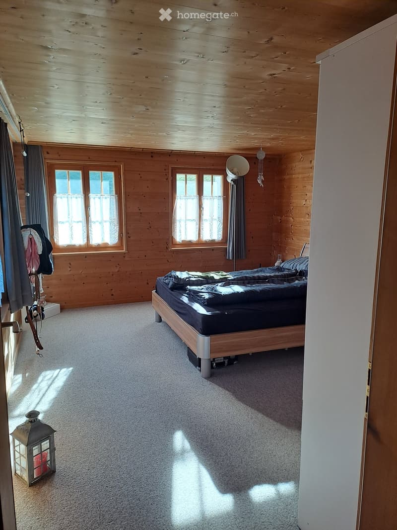 Cozy wooden bedroom with a large bed, wooden walls, large windows with curtains, and a lantern on the floor.