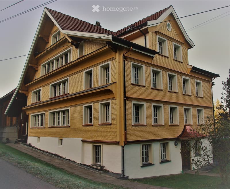 Two-story yellow house with multiple windows, red-tiled roof, and white trim around windows and roofline.