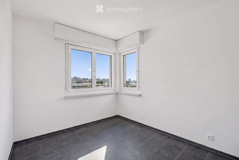 Empty room with white walls, dark tiled floor, and large windows offering a view of the outside. No furniture or equipment is present.