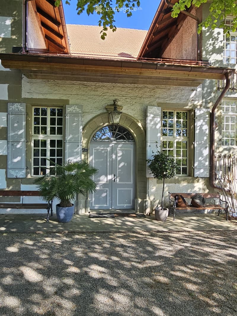 Traditional house, white exterior, arched entrance, white shutters, two benches, two potted plants, lamp above the door