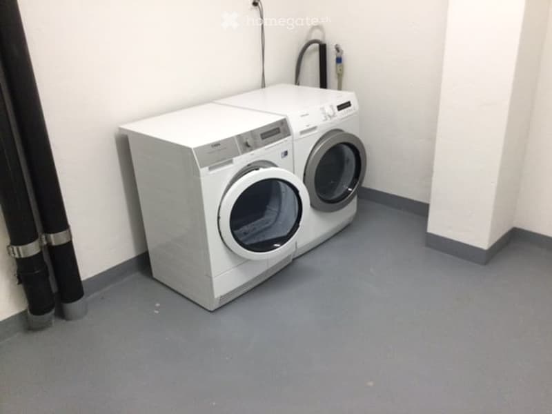A small, clean utility room with a white washing machine and dryer, grey flooring, and white walls.