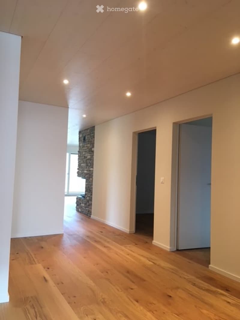 Empty room with wooden flooring, white walls, and recessed lighting. Features a stone accent wall and two doors leading to other spaces.