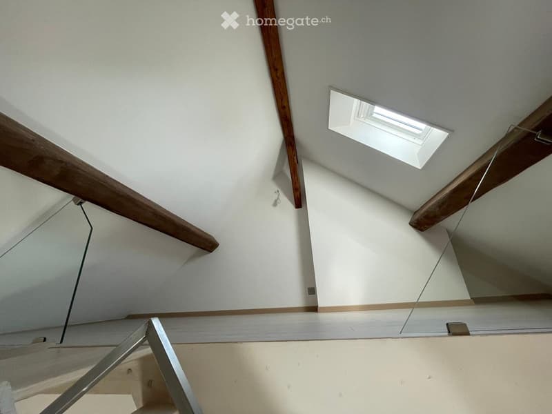 Empty hallway with exposed wooden beams, white walls, and a skylight window providing natural light.