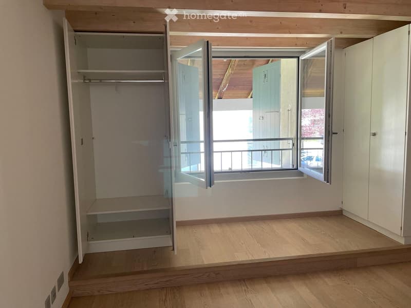 Empty room with wooden flooring, built-in closet with open shelves, and large window with balcony access.
