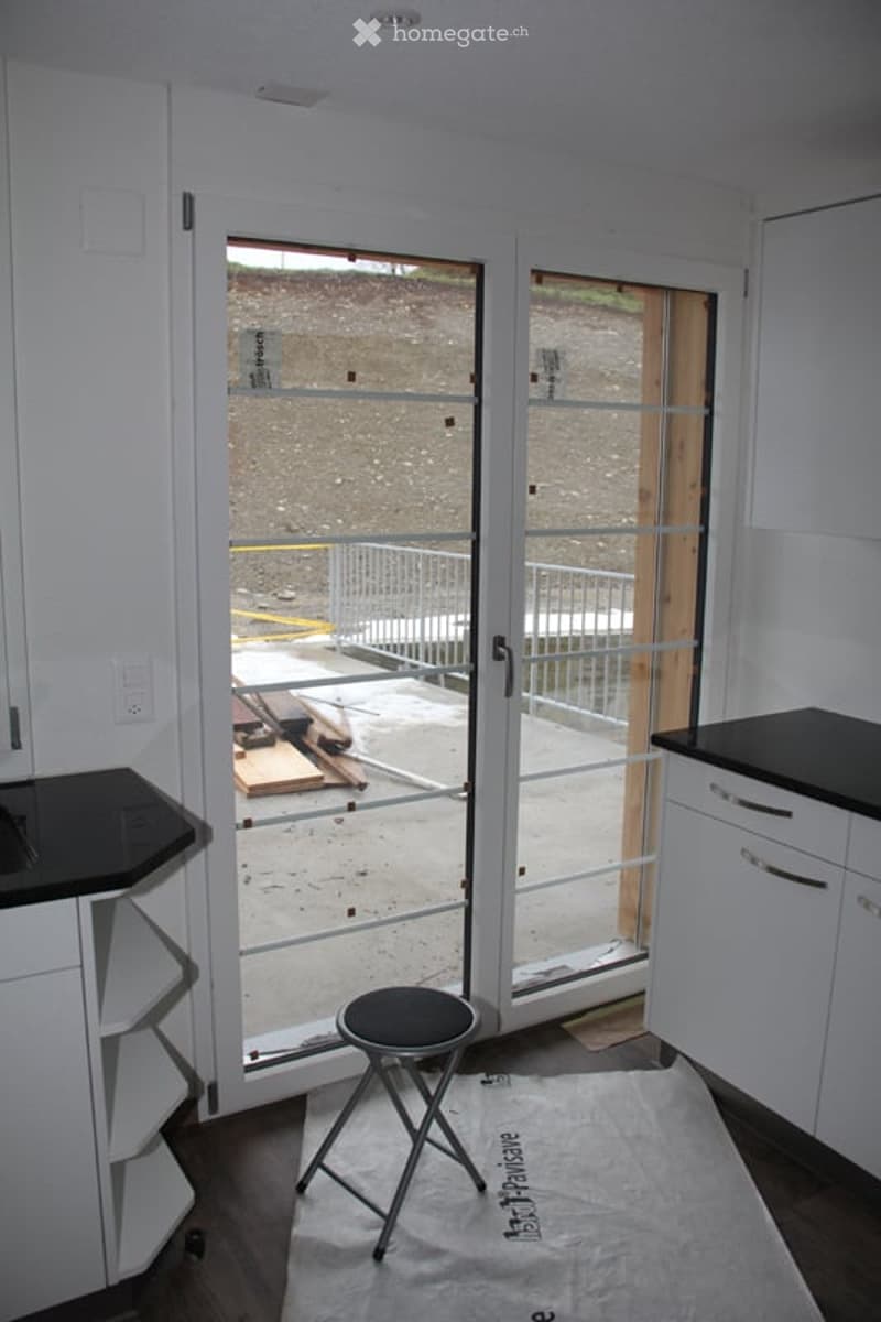 Empty room with white walls, dark countertops, a small black stool, and a large sliding glass door leading to an outdoor area.