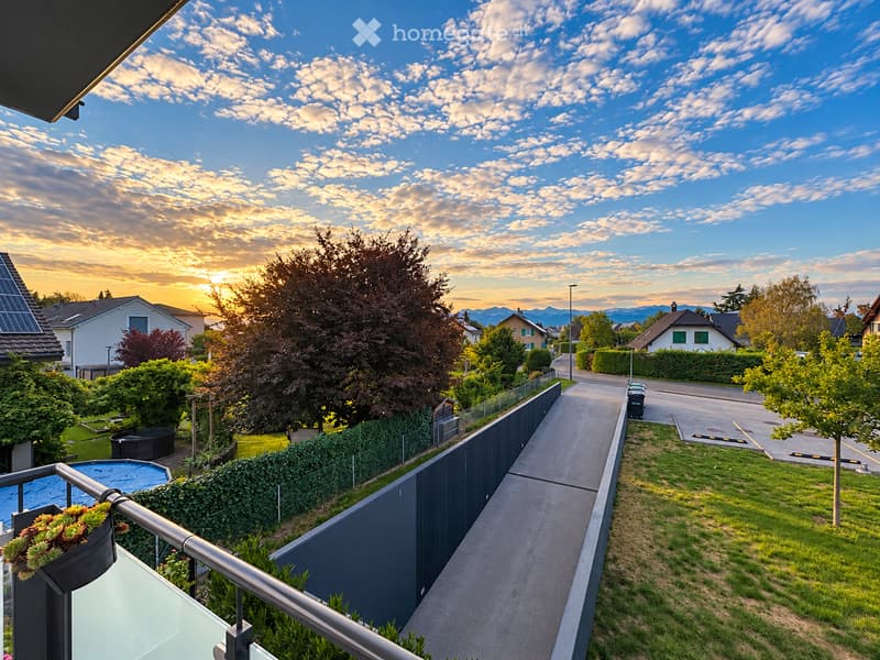 Balcony overlooking a residential neighborhood with a well-maintained garden, a swimming pool, and a pathway leading to the street.
