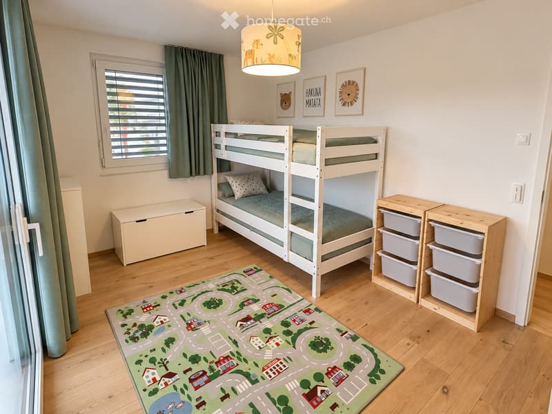 Cozy children's bedroom with a bunk bed, storage unit, colorful rug with road design, and framed artwork on the wall.